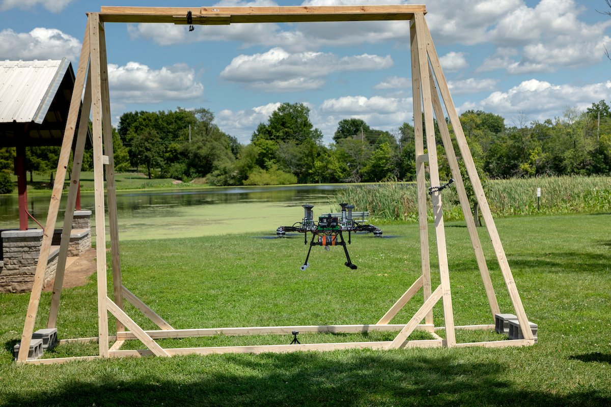 A quadcopter drone hovers inside a wooden testing frame on a sunny lawn